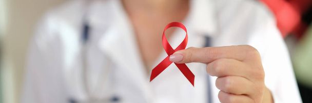 Close up of female doctor holds red ribbon in her hand as symbol of International AIDS Day, HIV awareness. - Photo, Image