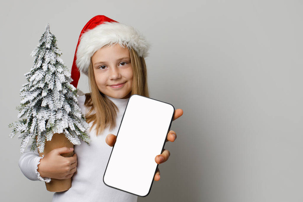 Christmas girl Santa holding smartphone with blank empty white screen display. Christmas concept - Photo, Image