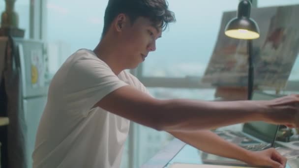 Inspirierter asiatischer Maler zeichnet Bild mit Aquarellfarbe und Pinsel, während er abends am Schreibtisch im Kreativatelier arbeitet - Filmmaterial, Video