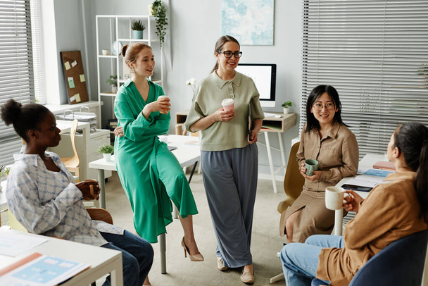 Skupina podnikatelek pije kávu a mluví spolu během přestávky na kávu v kanceláři - Fotografie, Obrázek