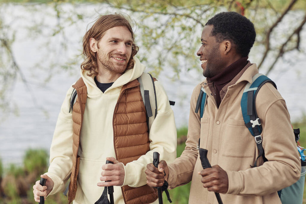 Двоє друзів з рюкзаками розмовляють один з одним під час прогулянки з палицями під час скандинавського алка на відкритому повітрі - Фото, зображення