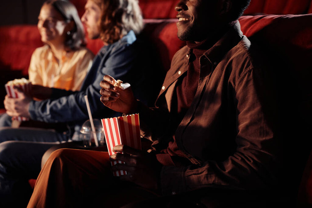 Afrikanischer junger Mann isst Popcorn und schaut mit seinen Freunden Film im Kino - Foto, Bild
