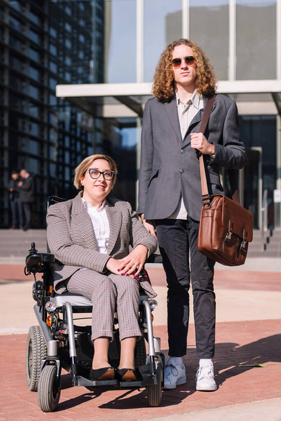 business man and woman using wheelchair posing happy looking at camera outdoors at financial district, concept of diversity and urban lifestyle - Photo, image