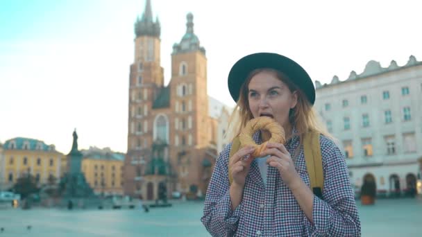 Giovane mano turistica femminile che tiene bagel, obwarzanek, pretzel. snack tradizionale polacco in Piazza del Mercato a Cracovia.  - Filmati, video