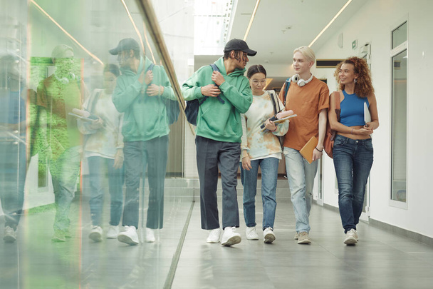 Divatos interkulturális tinédzser fiúk és lányok csoportja, akik a főiskola folyosóján mozognak órák után, és eldöntik, hová menjenek. - Fotó, kép