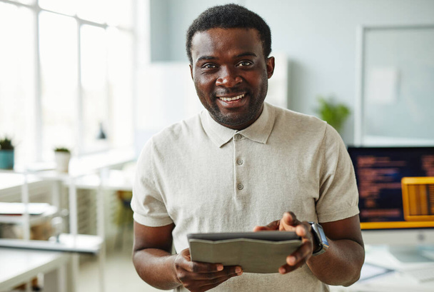 Portrét afrického IT specialisty usmívajícího se do kamery při použití digitálního tabletu stojící v kanceláři - Fotografie, Obrázek