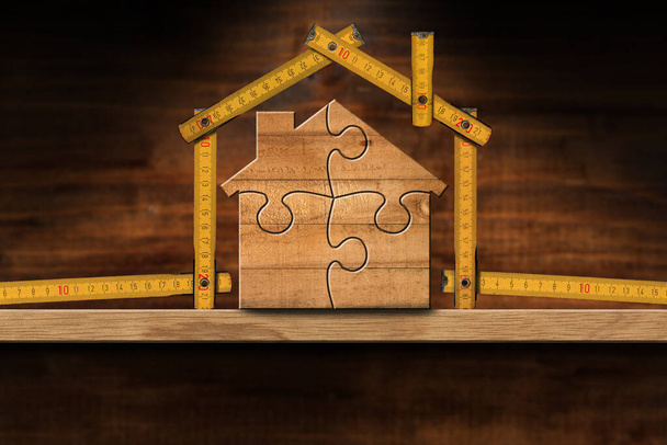Ξύλινο σπίτι από πτυσσόμενο χάρακα και κομμάτια παζλ, σε ξύλινο πάγκο εργασίας με χώρο αντιγραφής. Οικοδομική βιομηχανία και σχεδιασμός εσωτερικών χώρων. - Φωτογραφία, εικόνα