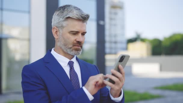 Ένας χαμογελαστός λευκός άνδρας, επιχειρηματίας και αφεντικό, δουλεύει στο σύγχρονο smartphone του έξω. Χρησιμοποιεί το τηλέφωνο για πλοήγηση, online συνομιλία, ανάγνωση μηνυμάτων και τραπεζικές δραστηριότητες εφαρμογών - Πλάνα, βίντεο