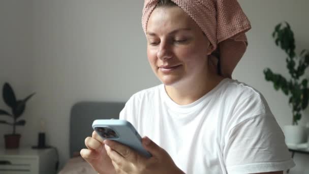 Nuori nainen käyttää t-paita pyjama sängyssä matkapuhelimen luottokortilla ostoksia verkossa loput rentoutua viettää aikaa makuuhuoneessa. Laadukas FullHD kuvamateriaalia - Materiaali, video