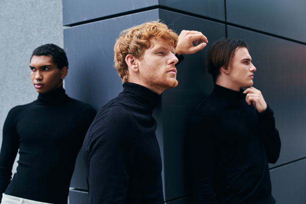 attractive pensive men in stylish black turtlenecks posing and looking away with wall backdrop - Photo, Image