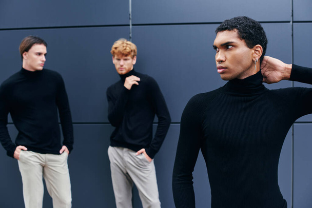 drie multiraciale jonge mannen in elegante casual outfits staan aan de muur, mode concept - Foto, afbeelding
