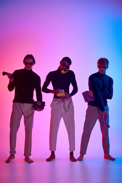 beaux modèles masculins multiethniques entourés de néons posant avec des téléphones fixes, hommes puissance - Photo, image
