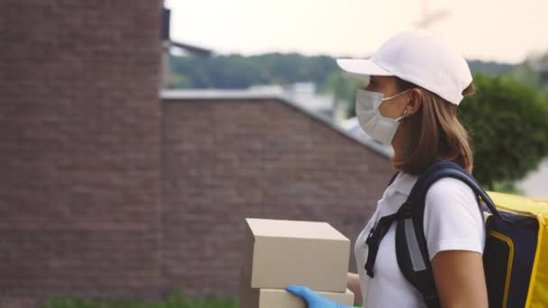 Un livreur féminin portant un masque protecteur et des gants livre une boîte en papier, portant un masque médical, des gants de sécurité et un uniforme. Délivrer une femme qui appelle l'interphone - Séquence, vidéo