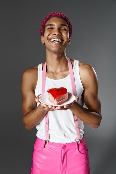 cheerful young man holding heart shaped mini cake and smiling at camera, fashion and style - Photo, Image