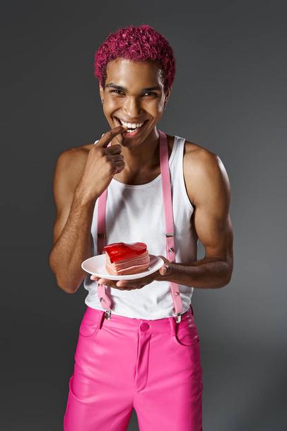 jolly african american man holding heart shaped mini cake and looking at camera, fashion and style - Photo, Image
