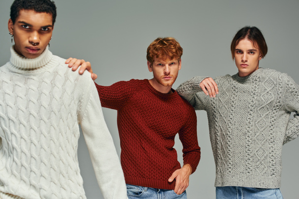 good looking diverse men in sweaters with hands on each others shoulders looking at camera, fashion - Photo, Image