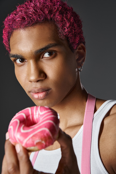 portret młodego Afroamerykanina z różowymi włosami pozowanie z różowym pączkiem, moda i styl - Zdjęcie, obraz