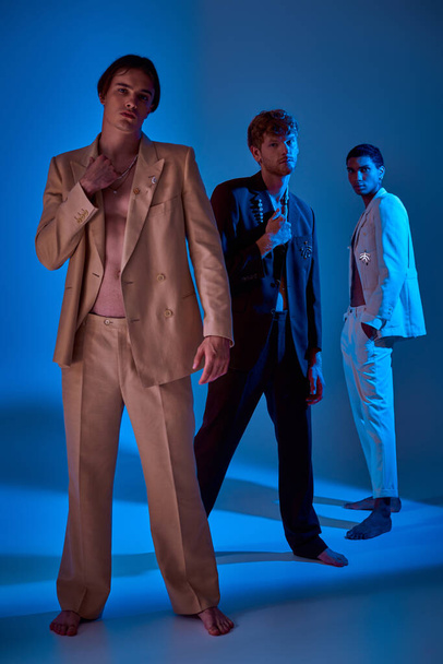 tiro vertical de los modelos masculinos con estilo joven en trajes elegantes con accesorios, luces azules, poder de los hombres - Foto, imagen