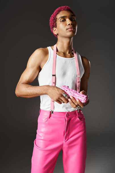 стильний рожевий чоловік позує харизматично з іграшковим пістолетом на сірому фоні, дивлячись на камеру - Фото, зображення