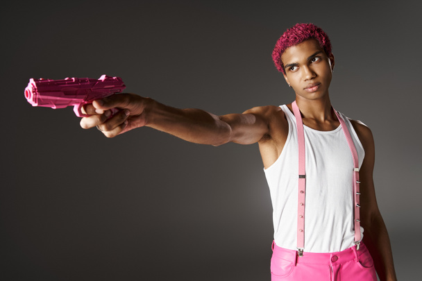 ハンサムピンクハイレッドスタイリッシュな男性 ピンクのズボン付きアクセサリー 彼のピンクのおもちゃ銃を脇に引っ張る - 写真・画像