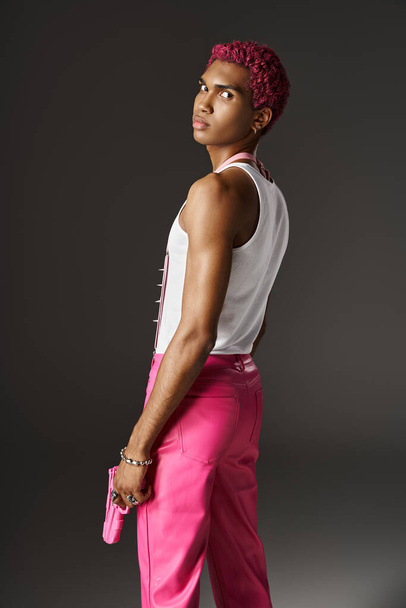 modelo masculino afroamericano serio en traje rosa vibrante posando con pistola de juguete sobre fondo gris - Foto, imagen