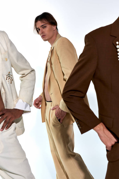 enfoque en el hombre joven en traje desabotonado posando junto a otros modelos masculinos sobre fondo gris - Foto, imagen