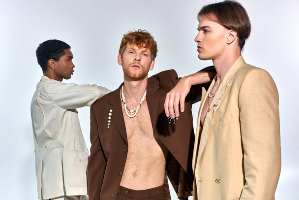 red haired bearded man looking at camera while other models posing in profile, fashion concept - Foto, Imagem