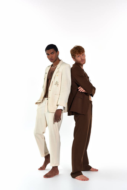 atractivo elegante dúo multirracial en trajes sexy posando espalda con espalda mirando a la cámara, poder de los hombres - Foto, imagen