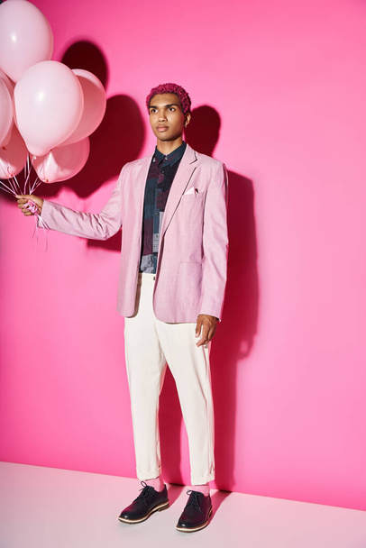 stylowy różowy mężczyzna model stoi nienaturalnie z balonami w rękach odwracając wzrok, lalka jak - Zdjęcie, obraz