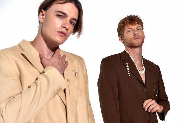 twee aantrekkelijke jonge mannen in elegante stijlvolle pakken met accessoires op zoek naar camera, mode concept - Foto, afbeelding