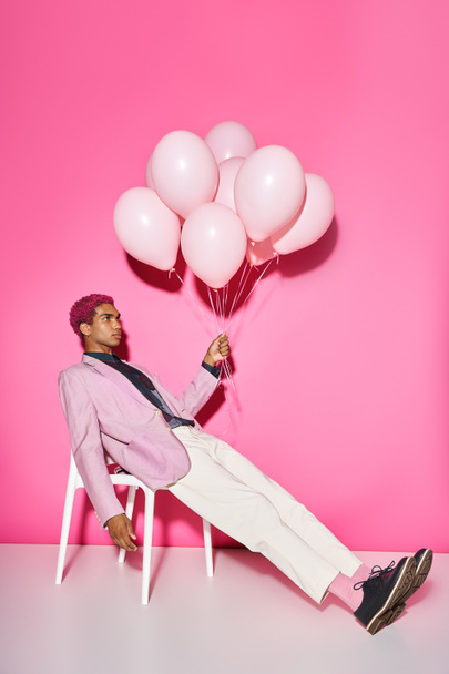 handsome young male model posing unnaturally with balloons in hand on pink backdrop, doll like - Photo, Image