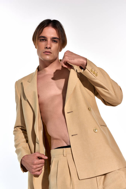 Düğmeleri iliklenmemiş takım elbiseli genç erkek modelin beyaz arka planda baştan çıkarıcı bir şekilde poz vermesi. - Fotoğraf, Görsel