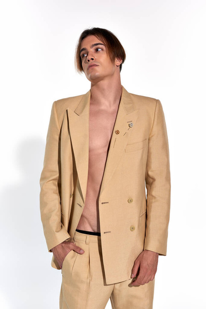 verticaal schot van knappe aantrekkelijke mannelijke model in beige sexy pak poseren op witte achtergrond, mode - Foto, afbeelding