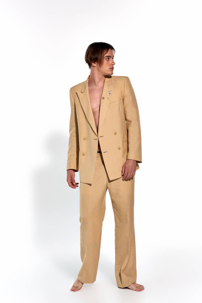 vertikale Aufnahme eines gut aussehenden, stylischen männlichen Modells im beigen Anzug, das barfuß posiert und wegschaut - Foto, Bild