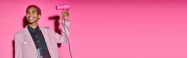 homem de cabelos rosa elegante sorrindo estranhamente com olhos fechados com secador de cabelo em suas mãos, banner - Foto, Imagem