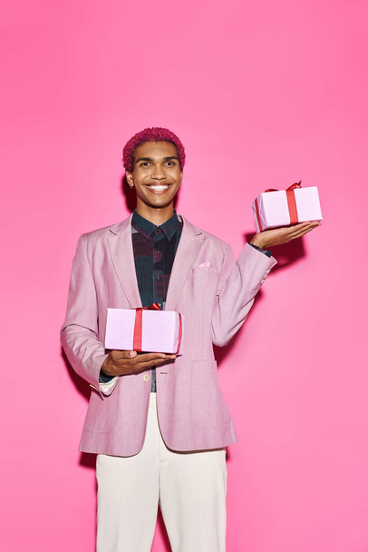 人形のように振る舞うピンクの背景に手でプレゼントをポーズする陽気な若い男性モデル - 写真・画像