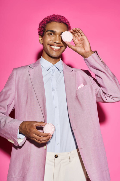 young stylish man smiling unnaturally and posing with zefir in his hands posing on pink backdrop - Photo, Image