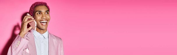stijlvol Afrikaans amerikaanse man praten per telefoon en onnatuurlijk glimlachen op roze achtergrond, banner - Foto, afbeelding