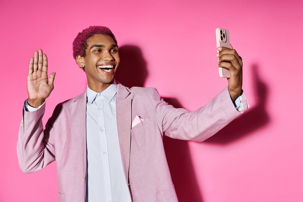 guapo joven posando anormalmente saludando a la cámara del teléfono móvil y sonriendo alegremente - Foto, Imagen