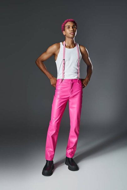 стильный красивый розовый волосы мужчина модель в штанах с подтяжками на сером фоне, концепция моды - Фото, изображение