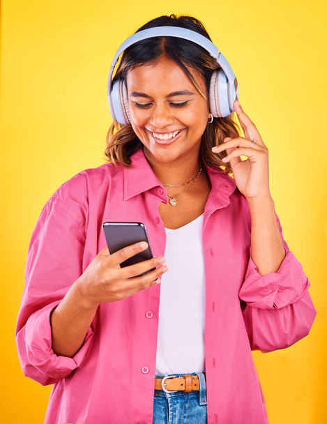 Kopfhörer, Handy und junge Frau im Studio, die Musik, Playlist oder Radio hört und vernetzt ist. Glückliches, telefonisches und weibliches Model aus Mexiko, das einen Song oder ein Album vor gelbem Hintergrund streamt - Foto, Bild
