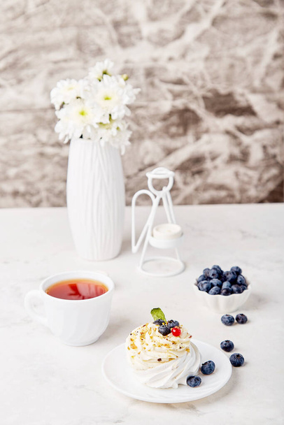 Traditionelles Pavlova Dessert mit Teetasse und Blaubeere. Herbstliche Teezeit-Stimmung im Hintergrund. Hygge-Ästhetik. Gemütliches Zuhause. - Foto, Bild