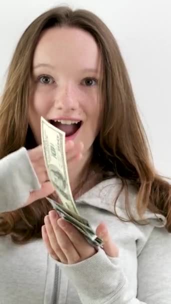 tyytyväinen onnellinen teini tyttö hajottaa 100 dollarin seteleitä eri suuntiin hidastettuna video valkoisella taustalla urheilutakki rikas mies heittää rahaa pois. Älä ajattele tulevaisuutta. - Materiaali, video