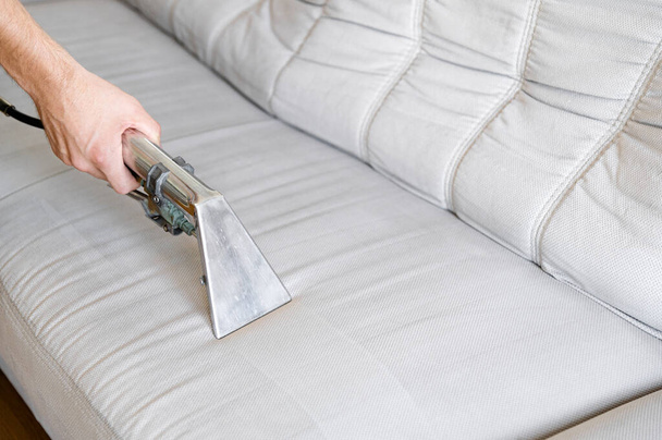 Professionally chemical cleaning. Cleaning concept. Man cleans sofa in the room, close up. Virus prevention sanitizing inside. The sofa is light gray or white.  - Photo, Image