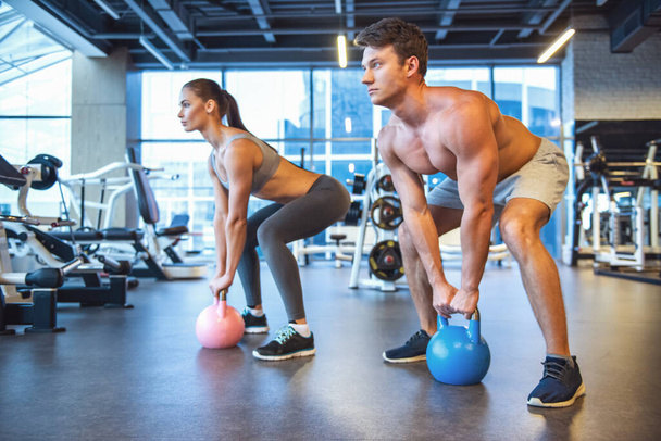 Attractive young sports people are working out with kettlebell in gym - Photo, Image