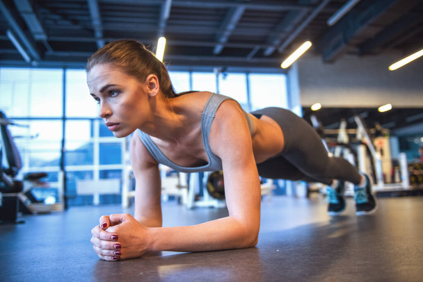 Attrayant jeune femme fait de l'exercice de planche tout en travaillant dans la salle de gym - Photo, image