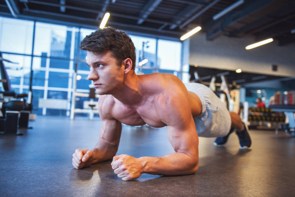 Atraente jovem homem muscular está fazendo exercício prancha enquanto se exercita no ginásio
 - Foto, Imagem