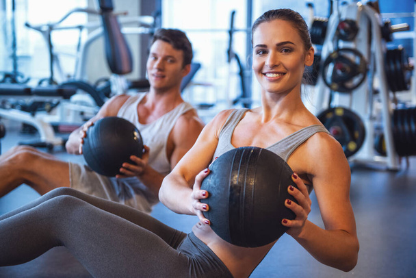 Atractivo joven musculoso hombre y mujer están haciendo ejercicio con bolas en el gimnasio
 - Foto, imagen