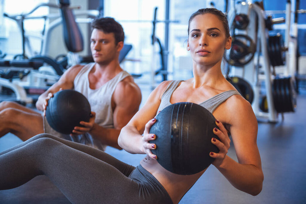 Atractivo joven musculoso hombre y mujer están haciendo ejercicio con bolas en el gimnasio
 - Foto, Imagen