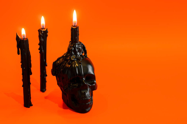 Zwarte schedel en kaarsen met vlam op oranje achtergrond. Halloween party concept. - Foto, afbeelding